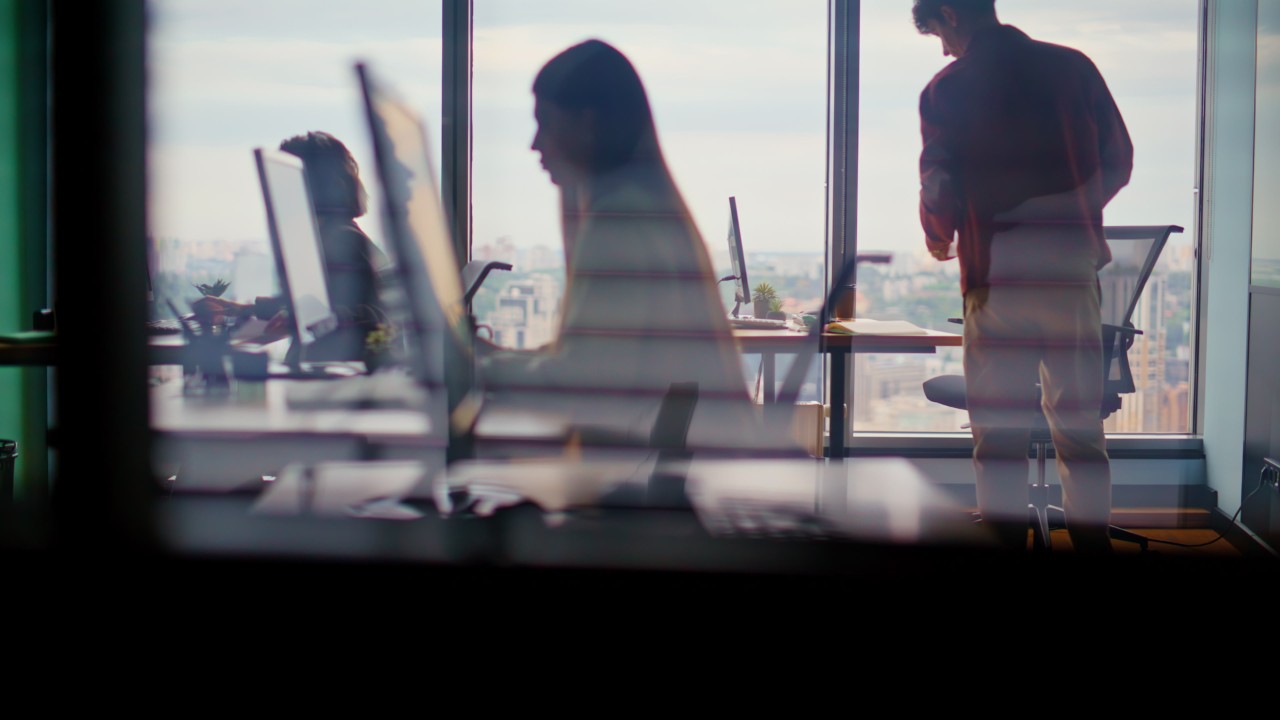 Corporate workers silhouettes typing computers in modern tech studio. Team of focused people debugging code. Open office with city panorama. Busy digital workflow and project development activities